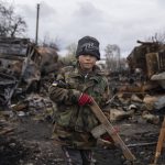 
              Yehor, 7, stands holding a wooden toy rifle next to destroyed Russian military vehicles near Chernihiv, Ukraine, Sunday, April 17, 2022. Witnesses said multiple explosions believed to be caused by missiles struck the western Ukrainian city of Lviv early Monday as the country was bracing for an all-out Russian assault in the east. (AP Photo/Evgeniy Maloletka)
            