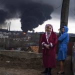 
              Women stay next to a car as smoke rises in the air in the background after shelling in Odesa, Ukraine, Sunday, April 3, 2022. (AP Photo/Petros Giannakouris)
            