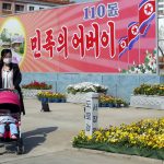 
              A woman pushes a baby on a stroller in front of the posters marking the 110th birth anniversary of late North Korean leader Kim Il Sung, in Pyongyang, DPRK, on Friday, April 15, 2022. The poster says "Father of Nation".  (AP Photo/Jon Chol Jin)
            