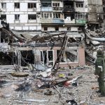 
              A serviceman stands at a building damaged during fighting in Mariupol, on the territory which is now under the Government of the Donetsk People's Republic control, eastern in Mariupol, Ukraine, Wednesday, April 13, 2022. (AP Photo/Alexei Alexandrov)
            