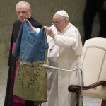 
              Pope Francis shows a flag that he said was brought to him from Bucha, Ukraine, during his weekly general audience in the Paul VI Hall, at the Vatican, Wednesday, April 6, 2022. (AP Photo/Alessandra Tarantino)
            