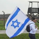 
              A man walks with Israeli flag at the Auschwitz Nazi concentration camp after the March of the Living annual observance that was not held for two years due to the global COVID-19 pandemic, in Oswiecim, Poland, Thursday, April 28, 2022. Only eight survivors and some 2,500 young Jews and non-Jews are taking part in the annual march that is scaled down this year because of the war in neighboring Ukraine that is fighting Russia's invasion. (AP Photo/Czarek Sokolowski)
            