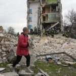 
              A woman carries her belongings as she leaves her house, background, ruined in the Russian shelling in Borodyanka, Ukraine, Wednesday, April 6, 2022. (AP Photo/Efrem Lukatsky)
            