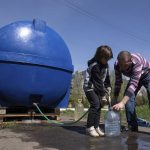 
              A girl Lisa helps a man to fill cans with water from a water tank installed for residents of Toretsk, eastern Ukraine, Monday, April 25, 2022. Toretsk residents have had no access to water for more than two months because of the war. (AP Photo/Evgeniy Maloletka)
            