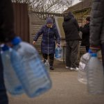 
              Local residents fill their bottles with the water they draw from a public fountain in Bucha, on the outskirts of Kyiv, on Monday, April 18, 2022. Citizens of Bucha are still without electricity, water and gas after more than 43 days since the Russian invasion began. (AP Photo/Emilio Morenatti)
            