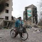 
              A man carries his belongings on a bike as he leaves his house, background, ruined in the Russian shelling in Borodyanka, Ukraine, Wednesday, April 6, 2022. (AP Photo/Efrem Lukatsky)
            