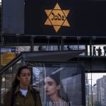 
              People walk along a bridge lit with a billboard showing a yellow Star of David that reads "Jude", Jew in German, resembling the one Jews were forced to wear in Nazi Germany, during the annual Holocaust Remembrance Day in Ramat Gan, Israel, Thursday, April 28, 2022. Israel marking the annual Day of Remembrance for the six million Jewish victims of the Nazi genocide who perished during World War II. (AP Photo/Oded Balilty)
            