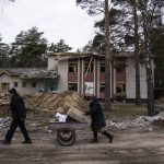 
              A man and his wife push a cart with food past a school damaged by shelling in Yahidne, near of Dnipro, Ukraine, Tuesday, April 12, 2022. (AP Photo/Evgeniy Maloletka)
            