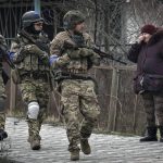 
              A woman looks at Ukrainian servicemen walking in the formerly Russian-occupied Kyiv suburb of Bucha, Ukraine, Saturday, April 2, 2022. As Russian forces pull back from Ukraine's capital region, retreating troops are creating a "catastrophic" situation for civilians by leaving mines around homes, abandoned equipment and "even the bodies of those killed," President Volodymyr Zelenskyy warned Saturday.(AP Photo/Vadim Ghirda)
            