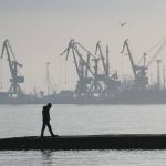 
              FILE - A man walks with harbor cranes in the background, at the trade port in Mariupol, Ukraine, Wednesday, Feb. 23, 2022. Russia began evacuating its embassy in Kyiv, and Ukraine urged its citizens to leave Russia. Unbroken by a Russian blockade and relentless bombardment, the key port of Mariupol is still holding out, a symbol of staunch Ukrainian resistance that has thwarted the Kremlin's invasion plans. (AP Photo/Sergei Grits, File)
            