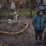 
              In the courtyard of their house, Vlad Tanyuk, 6, stands near the grave of his mother Ira Tanyuk, who died because of starvation and stress due to the war, on the outskirts of Kyiv, Ukraine, Monday, April 4, 2022. (AP Photo/Rodrigo Abd)
            
