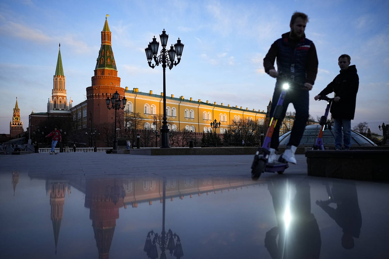 FILE - Youth ride scooters in Manezhnaya Square near Red Square and the Kremlin after sunset in Mos...