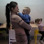 
              Marta Fedorova holds her baby boy as her son Volodymir 6, and her daughter Violetta 5, right, sit inside a school that is being used as a shelter for people who fled the war, in Dnipro city, Ukraine, on Tuesday, April 12, 2022. Marta Fedorova with her husband and five children fled from the city of Bahmud. (AP Photo/Petros Giannakouris)
            