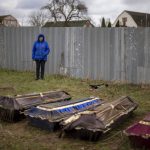 
              Ira Slepchenko, 54, stands next to coffins, one of them with the body of her husband Sasha Nedolezhko, 43, during an exhumation of a mass grave in Mykulychi, Ukraine on Sunday, April 17, 2022. All four bodies in the village grave were killed on the same street, on the same day. Their temporary caskets were together in a grave. On Sunday, two weeks after the soldiers disappeared, volunteers dug them up one by one to be taken to a morgue for investigation. (AP Photo/Emilio Morenatti)
            
