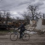 
              A man rides a bicycle past destroyed vehicles and an apartment building in Yahidne, near of Dnipro, Ukraine, Tuesday, April 12, 2022. (AP Photo/Evgeniy Maloletka)
            