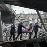 
              Ukrainian rescue workers carry an elderly woman under the destroyed bridge in Irpin, close to Kyiv close to Kyiv, Ukraine, Friday, April 1, 2022. Talks to stop the fighting in Ukraine resumed Friday, as another attempt to rescue civilians from the shattered and encircled city of Mariupol broke down and Russia accused the Ukrainians of a cross-border helicopter attack on an oil depot. (AP Photo/Efrem Lukatsky)
            