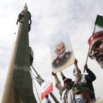 A demonstrator holds a poster of the late Iranian Revolutionary Guard Gen. Qassem Soleimani, who was killed in Iraq in a U.S. drone attack in early January 2020, in front of a Shahab-3 missile during the annual pro-Palestinian Al-Quds, or Jerusalem, Day rally in Tehran, Iran, Friday, April 29, 2022. Iran does not recognize Israel and supports Hamas and Hezbollah, militant groups that oppose it. (AP Photo/Vahid Salemi)