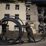 
              Municipal workers prepare a new tube to restore water supply in front of the building damaged by a Russian attack in Bahmut, Ukraine, on Thursday, May 12, 2022. (AP Photo/Evgeniy Maloletka)
            