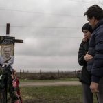
              Yura Nechyporenko, 15, hugs his uncle Andriy Nechyporenko above the grave of his father Ruslan Nechyporenko at the cemetery in Bucha, on the outskirts of Kyiv, Ukraine, on Thursday, April 21, 2022. The teen survived an attempted killing by Russian soldiers while his father was killed, and now his family seeks justice. (AP Photo/Petros Giannakouris)
            