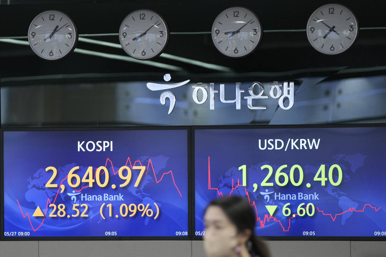 A currency trader walks by the screens showing the Korea Composite Stock Price Index (KOSPI), left,...