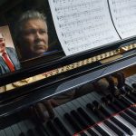 
              A photo of Neil Lawyer sits on the piano as his son, David Lawyer, plays in his home in Bellevue, Wash., Sunday, March 20, 2022. When the elder Lawyer died of complications from COVID-19 on March 8, 2020, the U.S. toll stood at 30, according to the CDC. At weddings, he joined his sons to serenade brides and grooms in a makeshift ensemble dubbed the Moose-Tones. Last October, when one of his granddaughters married, it marked the first family affair without Lawyer there to hold court. The Moose-Tones went on without him. "He would have just been beaming because, you know, it was the most important thing in the world to him late in life, to get together with family," David says. "I can honestly tell you he was terribly missed." (AP Photo/David Goldman)
            