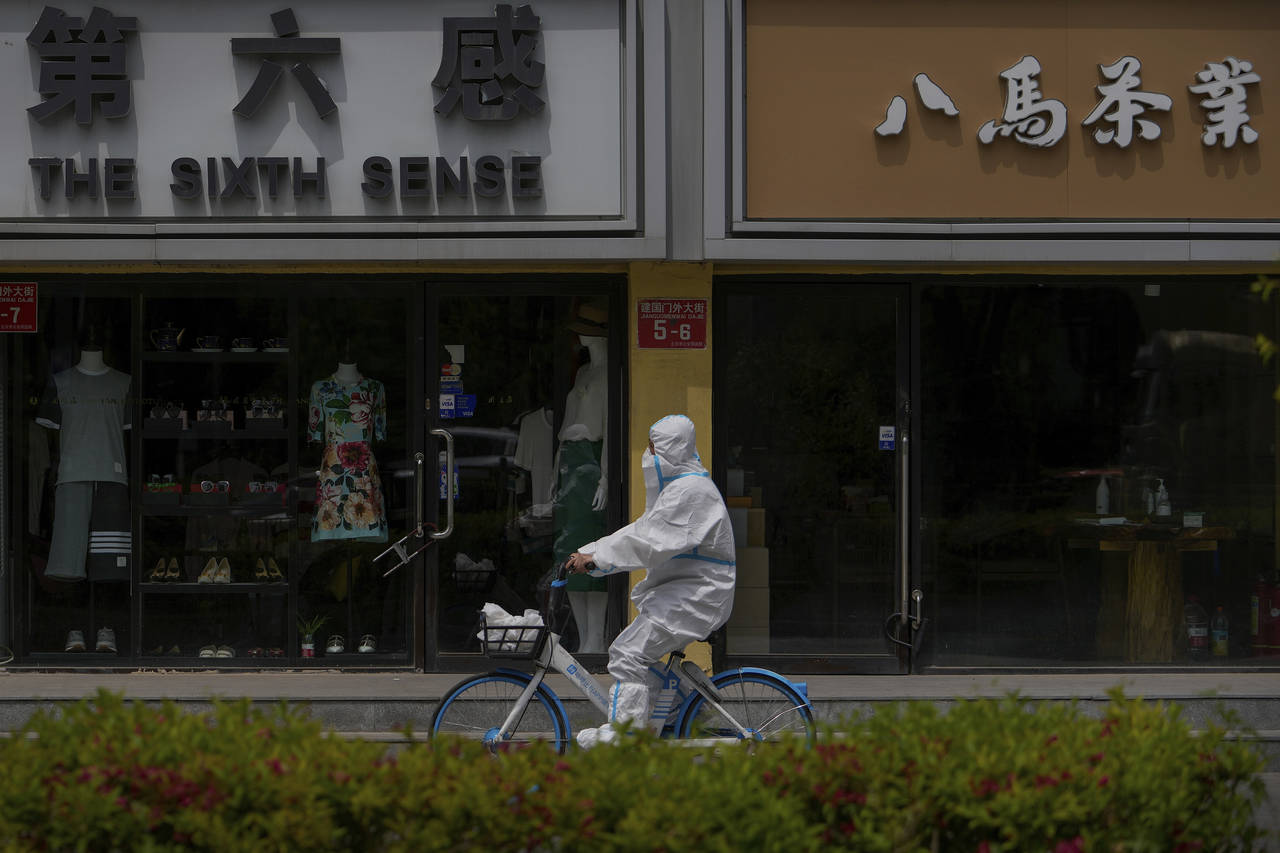 A worker in a protective suit rides a bicycle past shuttered retail shops after authorities ordered...