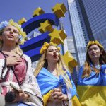 
              Women with flower decorations around their heads sing the Ukrainian national anthem below the Euro Monument during a demonstration under the slogan "Mothers against the war in Ukraine and Europe", in Frankfurt, Germany, Sunday, May 8, 2022. (Frank Rumpenhorst/dpa via AP)
            