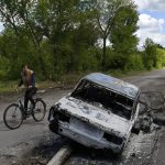 
              A man rides a bicycle past a car destroyed by shelling in a street in the village of Niu-York, Donetsk region, Ukraine, Monday, May 16, 2022. (AP Photo/Andriy Andriyenko)
            