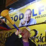 
              A supporter of Rodolfo Hernandez, presidential candidate with the Anti-corruption Governors League, blows a horn in front of campaign signs of the candidate on election night in Bogota, Colombia, Sunday, May 29, 2022. Hernandez will advance to a runoff contest in June after none of the six candidates in Sunday's first round got half the vote. (AP Photo/Leonardo Munoz)
            