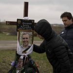 
              Yura Nechyporenko, 15, kisses the pictures of his father Ruslan Nechyporenko in front of his uncle Andriy Nechyporenko, at the cemetery in Bucha, on the outskirts of Kyiv, Ukraine, on Thursday, April 21, 2022. The teen survived an attempted killing by Russian soldiers while his father was killed, and now his family seeks justice. (AP Photo/Petros Giannakouris)
            