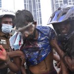 A Sri Lankan policeman, left, and a civilian helps an anti-government protester who was beaten up by government supporters during a clash in Colombo, Sri Lanka, Monday, May 9, 2022. Government supporters on Monday attacked protesters who have been camped outside the offices of Sri Lanka's president and prime minster, as trade unions began a "Week of Protests" demanding the government change and its president to step down over the country's worst economic crisis in memory. (AP Photo/Eranga Jayawardena)