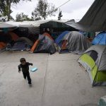 
              A boy from Honduras runs past tents set up at a shelter for migrants Friday, May 20, 2022, in Tijuana, Mexico. (AP Photo/Gregory Bull)
            