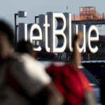 Travelers make their way near a JetBlue sign ahead of the Fourth of July holiday weekend at John F. Kennedy International Airport on Tuesday, June 28, 2022 in New York. (AP Photo/Julia Nikhinson)
