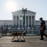 A Police officer leads a K9 around steel fencing and barricades surrounding the Supreme Court, Friday, June 24, 2022, in Washington. (AP Photo/Gemunu Amarasinghe)