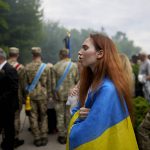 
              A woman wrapped in a Ukrainian flag attends the funeral of activist and soldier Roman Ratushnyi in Kyiv, Ukraine, Saturday, June 18, 2022. Ratushnyi died in a battle near Izyum, where Russian and Ukrainian troops are fighting for control of the area. (AP Photo/Natacha Pisarenko)
            