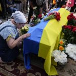 
              A woman kneels at activist and soldier Roman Ratushnyi's coffin during his memorial service in Kyiv, Ukraine, Saturday, June 18, 2022. Ratushnyi died in a battle near Izyum, where Russian and Ukrainian troops are fighting for control of the area. (AP Photo/Natacha Pisarenko)
            