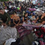 
              Eymar Hernandez and his wife Jenny Villamizar, sit with their children, Carlos, 14, Flor de los Angeles, 11, and Santiago, 3, sit on a concrete floor at a sports complex turned into a makeshift shelter, in Huixtla, Chiapas state, Mexico, Wednesday, June 8, 2022. The Hernandez’s who are part of an extended family of 18, including eight children, traveled from Venezuela to Mexico’s southern border in 15 days.  (AP Photo/Marco Ugarte)
            