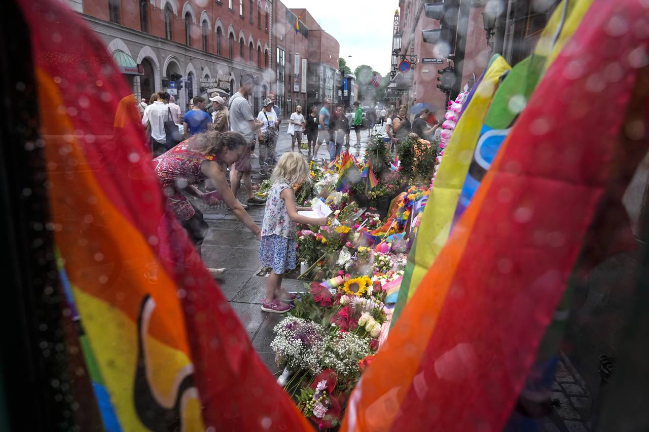 People lay flowers under the rain at the scene of a shooting in central of Oslo, Norway, Sunday, Ju...