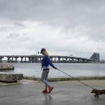A woman walks her dog during a brief pause of heavy rain, Saturday, June 4, 2022, in Miami. A tropical storm warning was in effect along portions of coastal Florida and the northwestern Bahamas. Several Miami streets were flooded and authorities were towing abandoned vehicles. (AP Photo/Marta Lavandier)