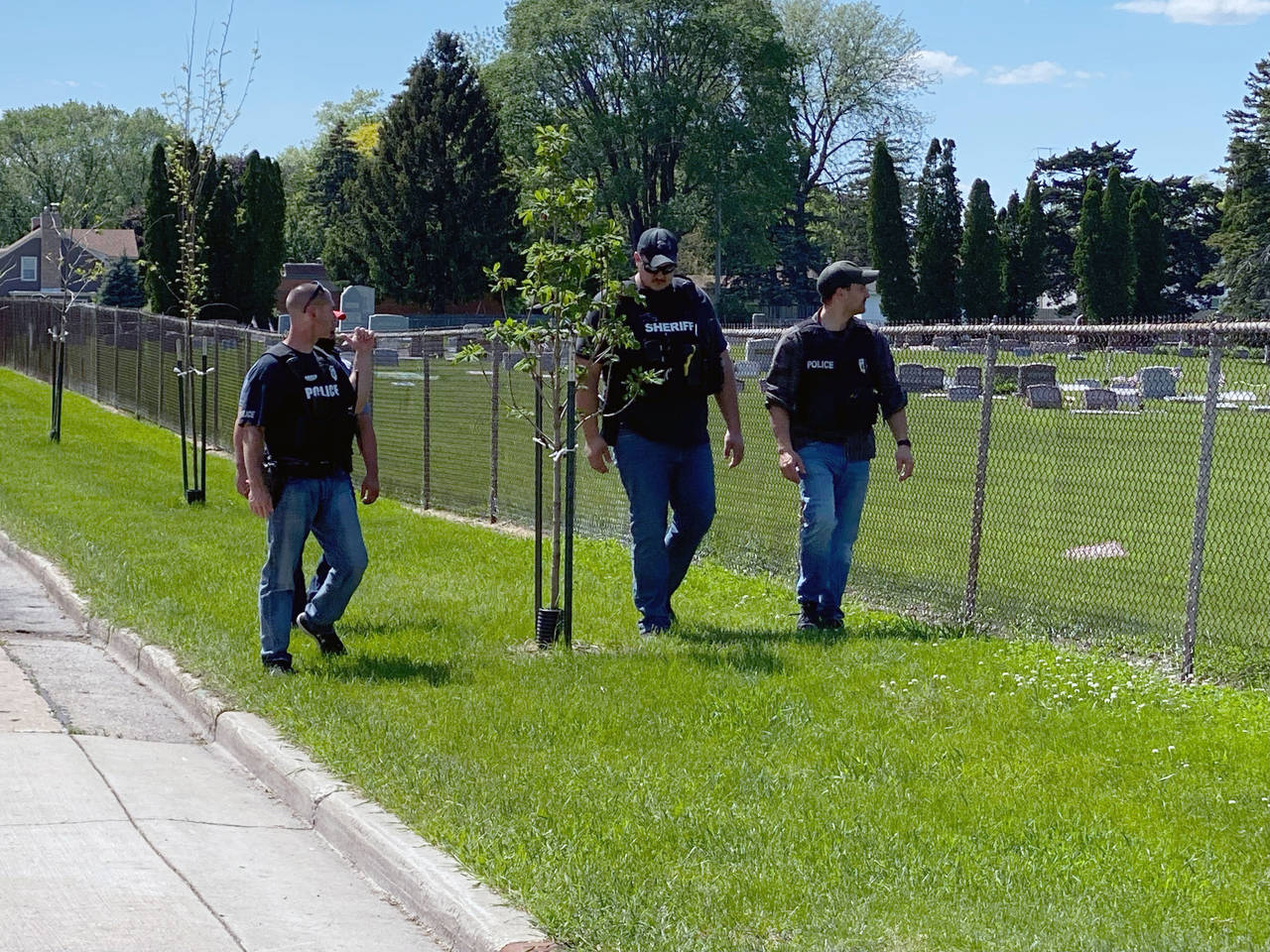Four law enforcement officers walk along the fence that borders Graceland Cemetery after shooting o...