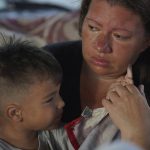 
              Venezuelan Jenny Villamizar, and her 3-year-old Santiago, who are part of a migrant caravan, sit inside a sports complex turned into a makeshift shelter, in Huixtla, Chiapas state, Mexico, Wednesday, June 8, 2022. The mother and son are part of an extended family of 18, including eight children, who traveled from Venezuela to Mexico’s southern border in 15 days. Venezuelans make up a large proportion of this caravan, the biggest of the year, in contrast to others in previous years. (AP Photo/Marco Ugarte)
            