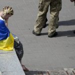 
              A woman sits at Maidan square during a memorial service for activist and soldier Roman Ratushnyi in Kyiv, Ukraine, Saturday, June 18, 2022. Ratushnyi died in a battle near Izyum, where Russian and Ukrainian troops are fighting for control the area.(AP Photo/Natacha Pisarenko)
            