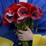 
              A woman wrapped in a Ukrainian flag holds flowers during the memorial service of activist and soldier Roman Ratushnyi in Kyiv, Ukraine, Saturday, June 18, 2022. Ratushnyi died in a battle near Izyum, where Russian and Ukrainian troops are fighting for control of the area. (AP Photo/Natacha Pisarenko)
            