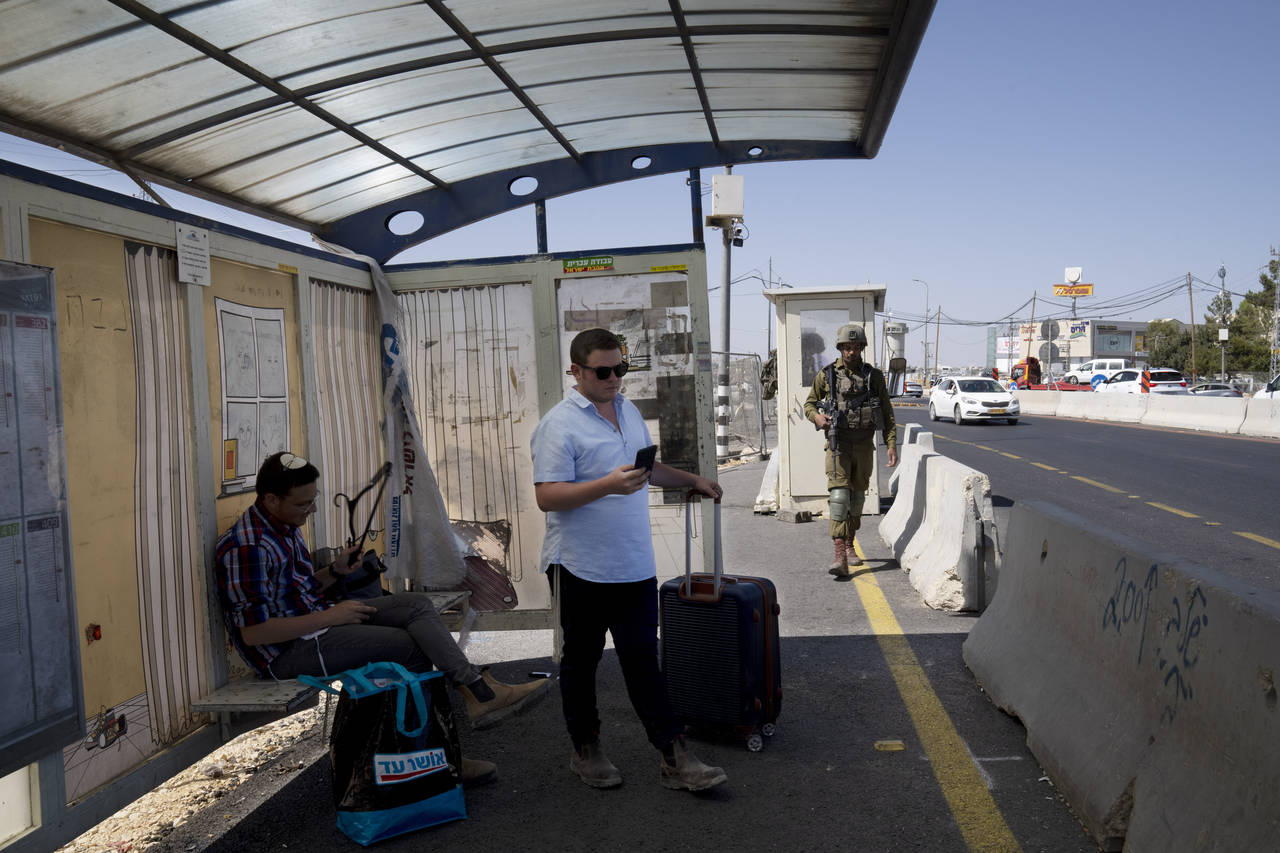 An Israeli soldier patrols a bus stop as settlers wait for a ride at the Gush Etzion junction, the ...