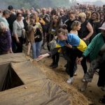 
              People throw sand on the coffin with the remains of activist and soldier Roman Ratushnyi during his funeral in Kyiv, Ukraine, Saturday, June 18, 2022. Ratushnyi died in a battle near Izyum, where Russian and Ukrainian troops are fighting for control of the area. (AP Photo/Natacha Pisarenko)
            