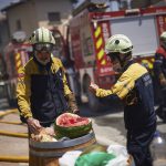 
              Firefighters eat watermelon during a break in San Martin de Unx in northern Spain, Sunday, June 19, 2022. Firefighters in Spain are struggling to contain wildfires in several parts of the country which as been suffering an unusual heat wave for this time of the year. (AP Photo/Miguel Oses)
            