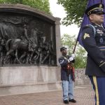 
              Civil War reenactor Larry Harris, of Philadelphia, center, holds a flag near the Robert Gould Shaw and the 54th Massachusetts Regiment Memorial, left, that commemorates the famed Civil War unit made up of Black soldiers, during re-dedication ceremonies of the memorial on the Boston Common, Wednesday, June 1, 2022, in Boston. The celebration comes on the 125th anniversary of the original unveiling of the bronze relief, which is considered the nation's first honoring Black soldiers. (AP Photo/Steven Senne)
            