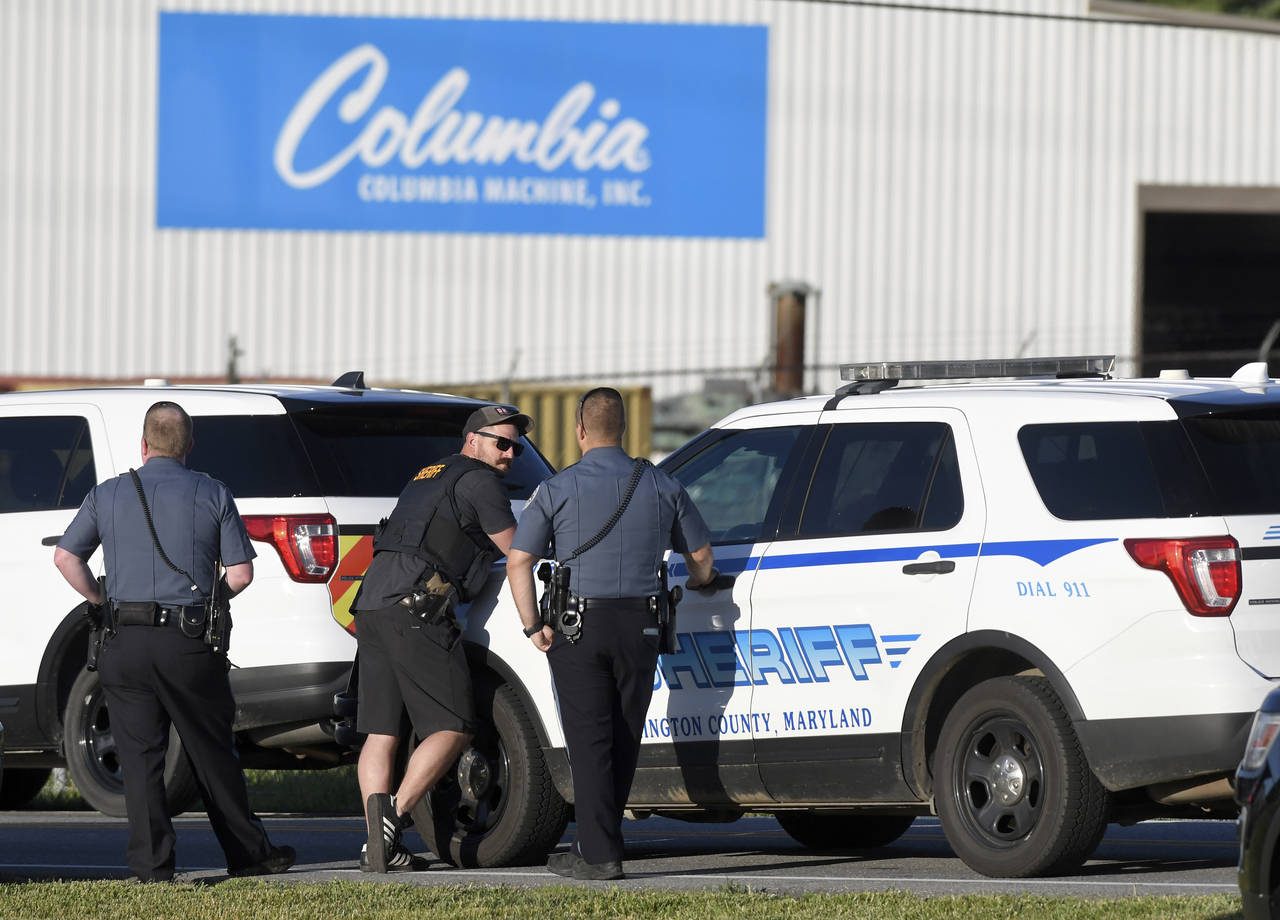 Police stand near where a man opened fire at a business, killing three people before the suspect an...