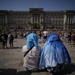 
              People sit covering their heads from the sun after a scaled down version of the Changing of the Guard ceremony took place outside Buckingham Palace, during hot weather in London, Monday, July 18, 2022. Britain's first-ever extreme heat warning is in effect for large parts of England as hot, dry weather that has scorched mainland Europe for the past week moves north, disrupting travel, health care and schools. (AP Photo/Matt Dunham)
            