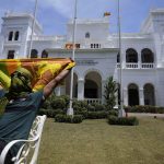 
              A protester holding a national flag stretches as he sits in the lawn of prime minister Ranil Wickremesinghe's office while preparing to vacate the building with other protesters in Colombo, Sri Lanka, Thursday, July 14, 2022. (AP Photo/Eranga Jayawardena)
            